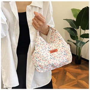Floral canvas handbag held by model featuring orange leather patch and strawberry logo