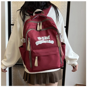 Detail view of burgundy nylon backpack with SIM SIJIMIAO lettering and beige straps