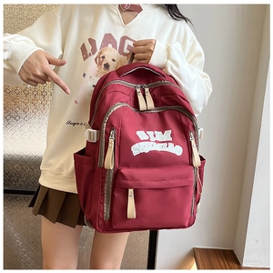 Detail of red nylon backpack with Sim Simmao lettering showing daily use on model