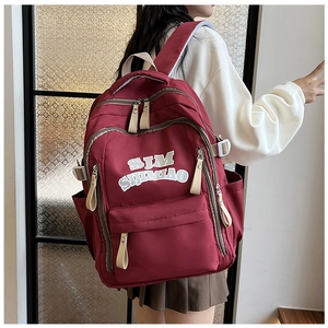 Detail view of burgundy canvas backpack with SJM letter print worn by a fashion model