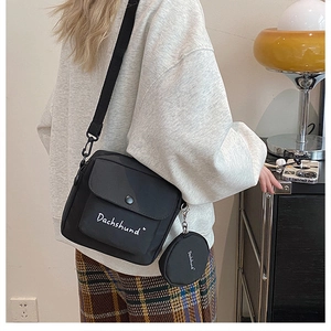 Detail of black canvas crossbody bag with small round coin purse and white text lettering