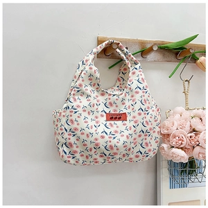 Detail of floral canvas handbag with red logo tag on a minimalist wooden hanger