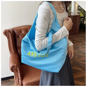 Detalle del bolso tote azul de gran capacidad con letras amarillas llevado por modelo