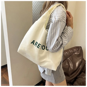 Detalle del bolso tote de lona crema con letras verdes apoyado en un sofá marrón