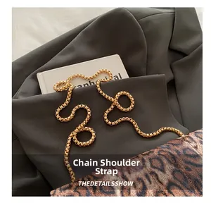 Détail de la bandoulière chaîne dorée sur sac léopard posé sur un costume gris