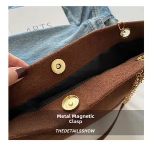 Détail d'un sac bandoulière en daim marron avec boucle magnétique dorée et chaîne