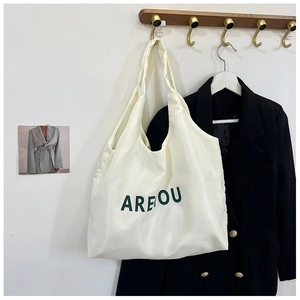 Detalle del bolso tote blanco roto con letras verdes colgado de un gancho dorado