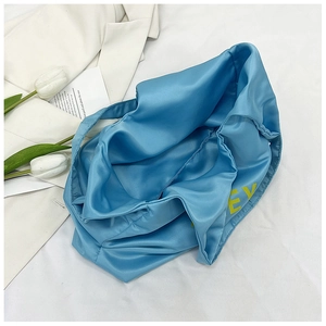 Detalle del bolso tote de satén azul con textura sedosa y estampado de letras amarillas