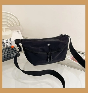 Close-up of black crossbody bag with white QK logo and adjustable strap on a modern desk