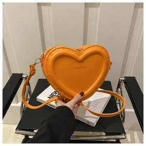 Detail of a bright orange heart-shaped crossbody bag with gold fashion lettering