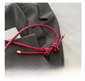 Détail d'une bandoulière rouge à motif crocodile avec embouts dorés et nœud décoratif
