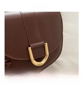Close-up of brown leather saddle bag featuring a stylish golden horseshoe metal buckle