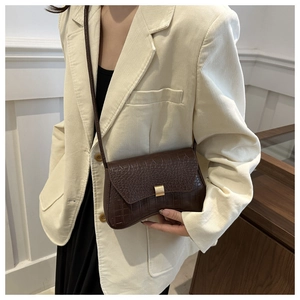 Détail d'un sac bandoulière marron foncé texture crocodile avec boucle dorée sur un mannequin