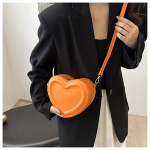 Close-up of bright orange heart-shaped leather crossbody bag with adjustable shoulder strap
