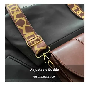 Detail of adjustable patterned textile strap with gold metal buckle on brown saddle bag