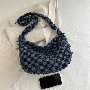 Blue denim checkerboard tote bag with distressed fringes on a white blazer background