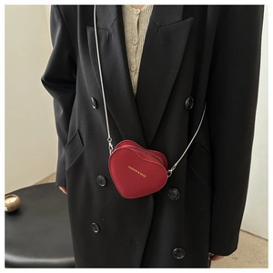 Gros plan sur le mini sac cœur rouge en cuir avec texte doré et bandoulière chaîne argent
