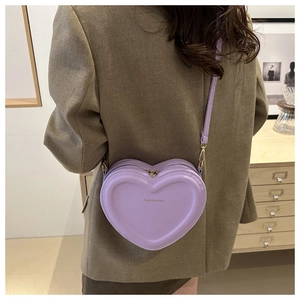 Detail of light purple heart-shaped crossbody bag worn by a model in a cozy indoor setting