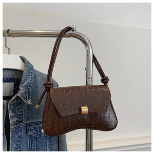 Gros plan sur la texture crocodile marron foncé et le fermoir métallique doré mat du sac