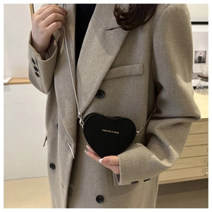 Détail d'un sac bandoulière en forme de cœur sur un blazer beige avec chaîne