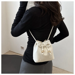 Rear view of model wearing white woven bucket bag with drawstring and gold metal beads