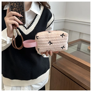 Detail of pink quilted cosmetic bag featuring embroidered black bows and wrist strap