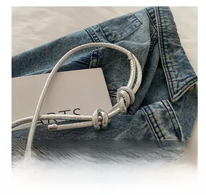 Silver crescent bag detail showing woven rope shoulder strap over denim jacket texture