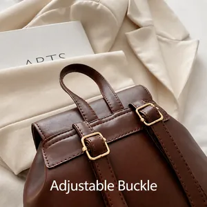 Detail view of adjustable leather straps with gold buckles on a dark brown backpack