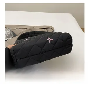Primer plano del bolso tipo cubo acolchado negro con bordado de lazo rosa y base firme
