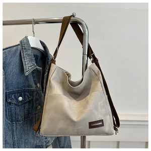 Detail of grey PU leather tote bag with brown fabric strap and fashion label on hanger