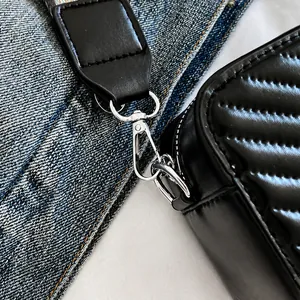 Detail van zilveren karabijnsluiting en gestreepte riem op zwarte gewatteerde tas