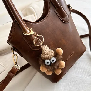 Detail of a brown leather handbag with a cute plush charm and gold hardware accents