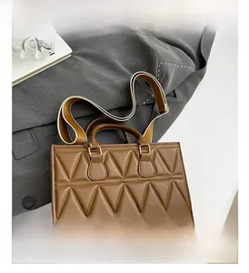 Detail of caramel quilted crossbody bag featuring a wide woven strap on a grey suit