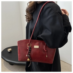 Detail of burgundy vintage tote bag with metal logo and bell charm on a black outfit