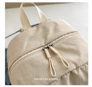 Detail view of smooth double zippers and woven handle on beige nylon backpack