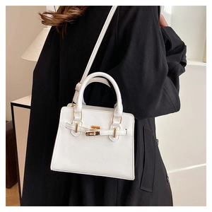 Detailed view of white trapezoid handbag with gold clasp on black coat