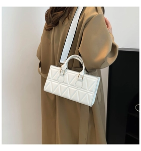 Detail of white geometric quilted leather handbag styled with a wide woven shoulder strap