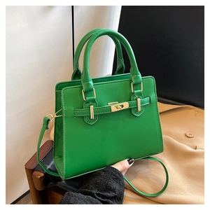 Detail of green structured handbag featuring gold metal turn-lock and buckle strap design
