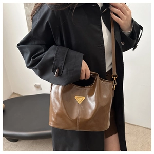 Detail of glossy chocolate brown bucket bag with triangular metal plate and slim strap