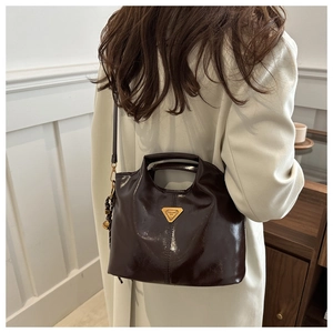 Detail of dark brown patent leather bucket bag with gold triangle plaque and strap