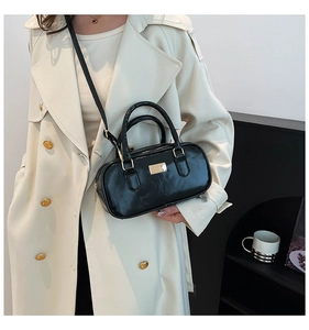 Détail d'un sac cylindrique noir vintage avec plaque dorée et bandoulière amovible