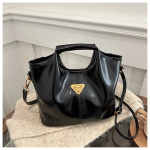 Detailed view of black patent leather bag with gold triangular logo on a wooden desk
