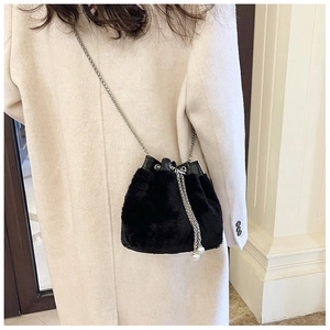 Détail d'un sac seau noir en peluche avec chaîne argentée porté sur un manteau d'hiver