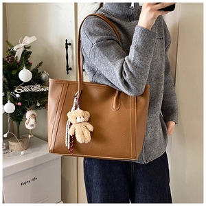 Brown litchi grain tote bag detail with cute plush bear charm and striped scarf accessory