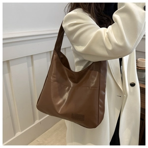 Dettaglio borsa hobo in pelle marrone con ampia tracolla e logo MIMIBO indossata dal modello