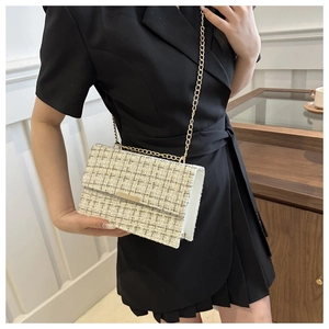 Detail of tweed flap bag with gold chain strap worn over a black dress in a chic room