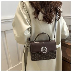Detail of a brown leather shoulder bag with vintage monogram and metal M logo on model