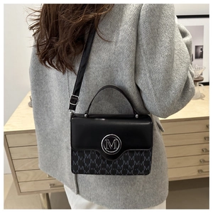 Detail of crossbody bag with black matte flap and grey M-patterned texture and silver logo