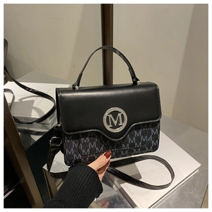 Detail of a vintage black leather crossbody bag featuring a silver M logo and monogram pattern