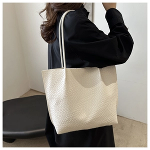 Close-up of beige woven tote bag worn on shoulder by a model in a black shirt